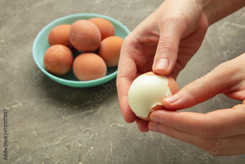 фотографія Woman peeling boiled egg on grey background, closeup