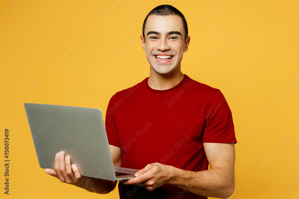 Young smiling happy IT middle eastern man wear red t-shirt casual clothes hold use work on laptop pc computer look camera isolated on plain yellow orange background studio portrait Lifestyle concept Young smiling happy IT middle eastern man wear red t-shirt casual clothes hold use work on laptop pc computer look camera isolated on plain yellow orange background studio portrait Lifestyle concept