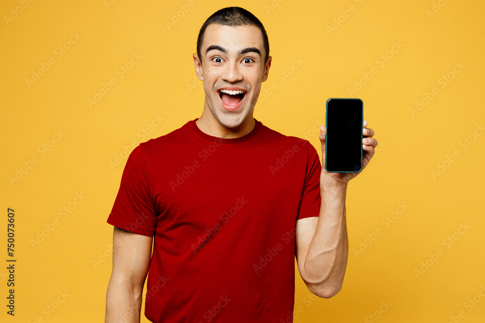 Young surprised middle eastern man he wear red t-shirt casual clothes hold in hand use mobile cell phone with blank screen workspace area isolated on plain yellow orange background. Lifestyle concept. Young surprised middle eastern man he wear red t-shirt casual clothes hold in hand use mobile cell phone with blank screen workspace area isolated on plain yellow orange background. Lifestyle concept.