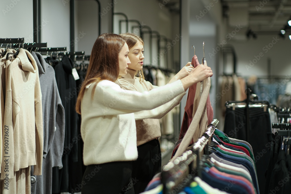 Portrait of smiling two young women shopping together in a boutique and choosing clothes. Two women in a mass market choose a dress and a blouse. Seasonal holiday discounts on purchases. Black Friday Portrait of smiling two young women shopping together in a boutique and choosing clothes. Two women in a mass market choose a dress and a blouse. Seasonal holiday discounts on purchases. Black Friday