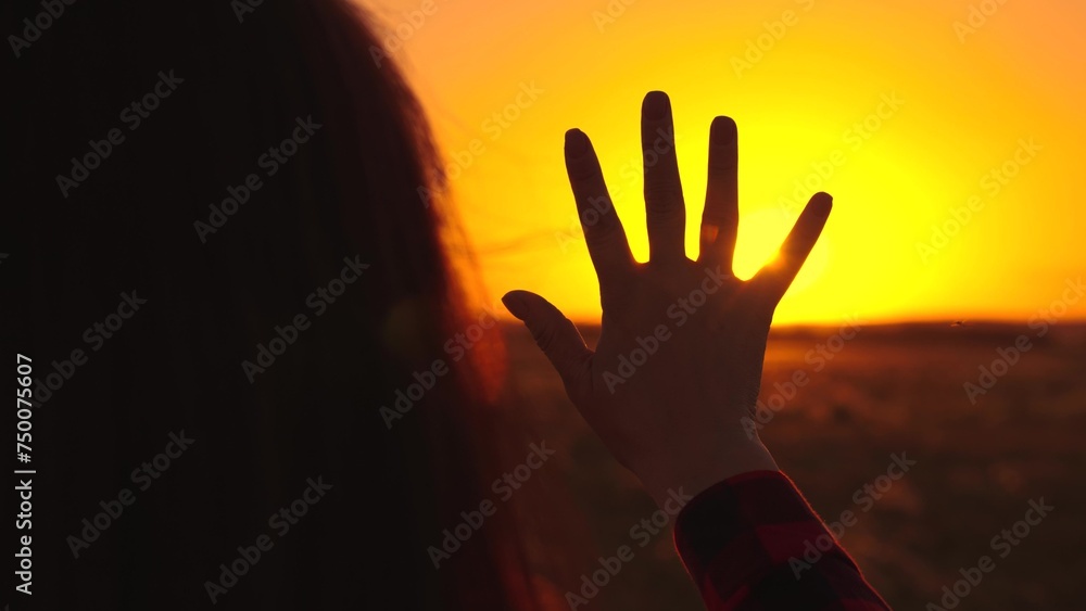 Young girl stretches out her hand to sun, dreams in nature. Sunrise in nature. Prayer in nature. Sunset, sun between fingers of girls hand. Hand of happy child girl at Sunset. Child play hand to sun