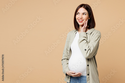 Young minded pregnant expectant woman future mom wear grey shirt stroking put hands on belly stomach tummy with baby look aside isolated on plain beige background. Maternity family pregnancy concept.