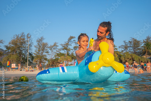.A boy plays with a water gun on a blue rubber ring in the shore. .He also enjoys the feeling of the rubber ring on the blue sea, .which provides a secure surface for him to play on.