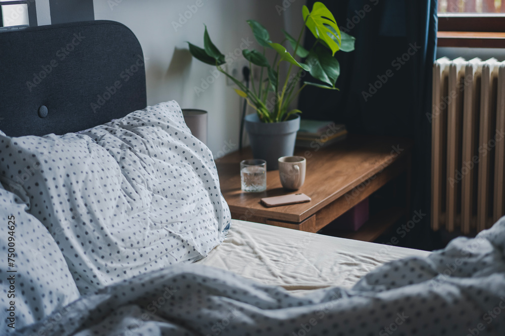 Cozy bed with white sheet at home with bedside table with smartphone and glass of water, morning time concept - obrazy, fototapety, plakaty 