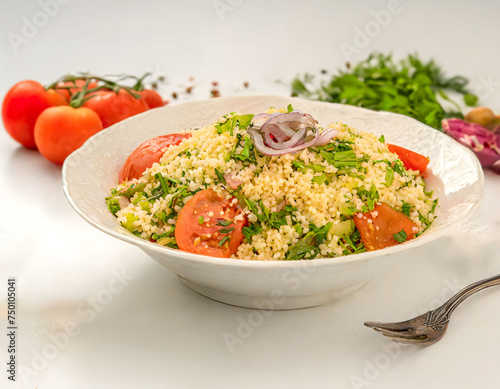 A vibrant bowl of fresh tabbouleh salad garnished with a sprig of mint, surrounded by ingredients like tomatoes and olive oil, set on a white surface.