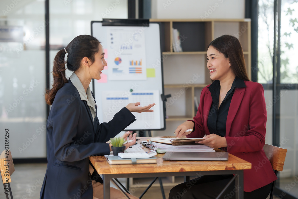 Two asian businesswomen discussing and reviewing documents in office. Professional workplace consultation. Corporate business and teamwork concept. Two asian businesswomen discussing and reviewing documents in office. Professional workplace consultation. Corporate business and teamwork concept.