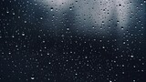 A black wet background, with raindrops overlaying a window, evokes the autumn weather, illustrating water drops on transparent glass.