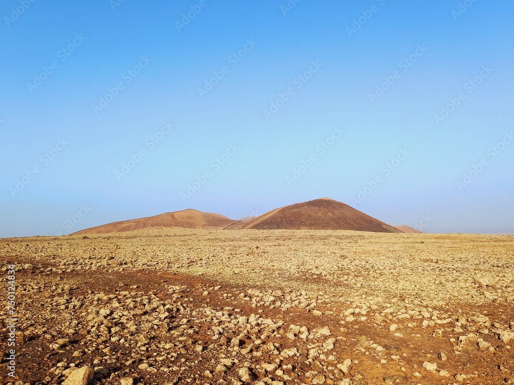 Volcanic landscape. Desert area with stones, rocks and sandstone and silhouette of volcano slopes on the horizon under blue sky. Landscapes and extreme nature.