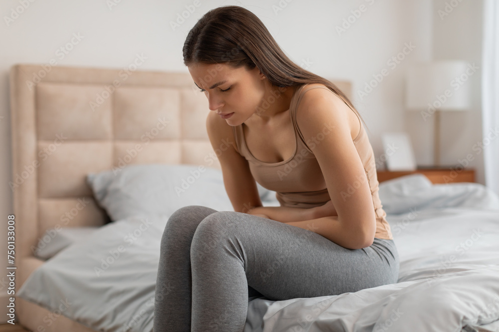 Woman with stomach ache sitting on bed, looking distressed