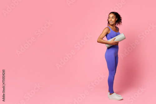 Athletic black lady holding foam roller standing on pink background