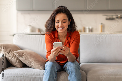 Smiling woman texting on her phone while relaxing on sofa