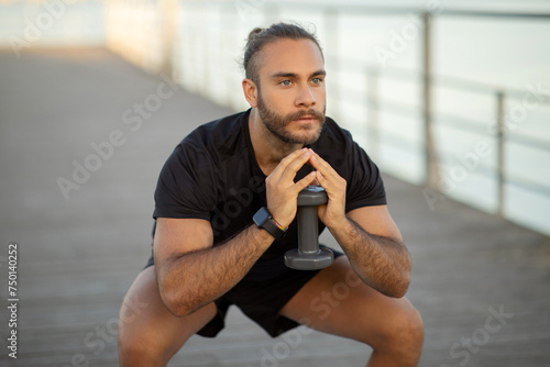 Athlete man performing squats holding dumbbell weights working out outside