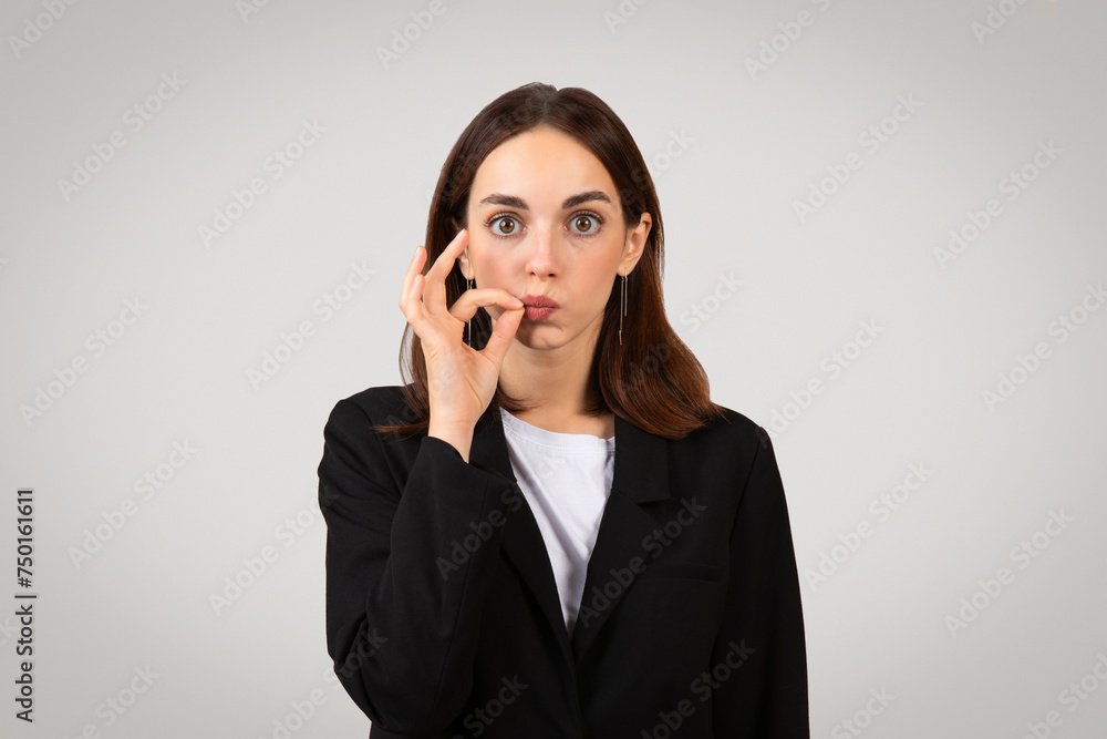 Playful businesswoman in a black suit making a funny face while gesturing a small amount with fingers Playful businesswoman in a black suit making a funny face while gesturing a small amount with fingers