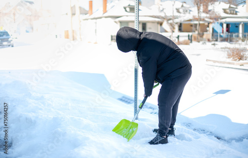 A man in a warm black jacket and trousers shoveling snow in front of their home for prepare the road for convenience.