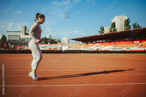 A sportswoman is running on running track on stadium.
