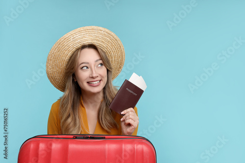 Happy young woman with passport, ticket and suitcase on light blue background, space for text
