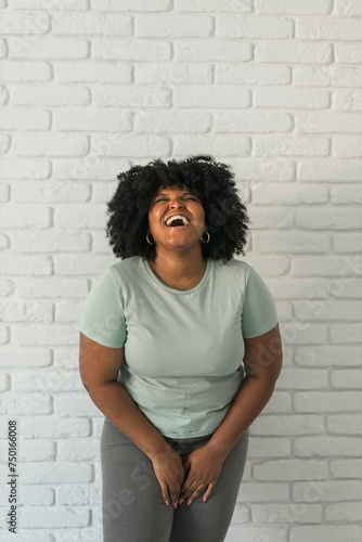 Laughing African American woman with an afro hairstyle and good sense of humor smiling and laugh on brick wall at home background. Copy space. Happiness and good emotions concept