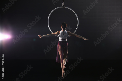 Young woman performing acrobatic element on aerial ring against dark background photo