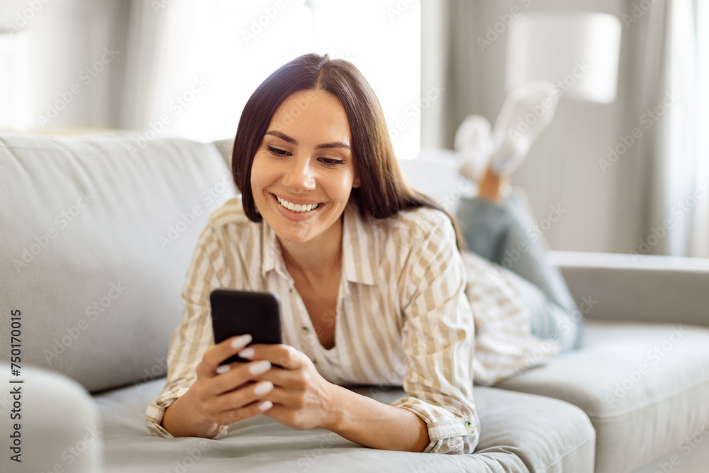 Happy young european lady messaging on smartphone while relaxing at home Happy young european lady messaging on smartphone while relaxing at home