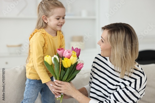 Little daughter congratulating her mom with bouquet of beautiful tulips at home. Happy Mother's Day