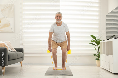 Fototapeta Naklejka Na Ścianę i Meble -  Senior man doing exercise with fitness elastic band on mat at home
