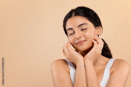 Sensual young indian woman with beautiful glowing skin posing against beige background