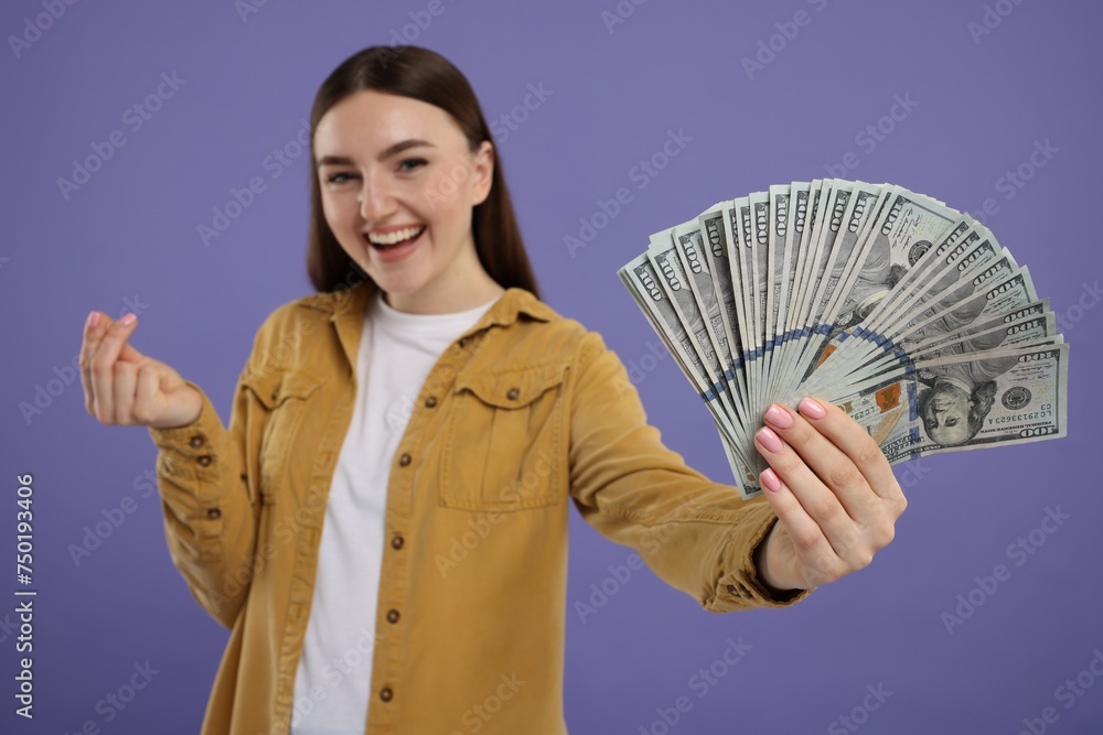 Happy woman with dollar banknotes showing money gesture on purple background, selective focus Happy woman with dollar banknotes showing money gesture on purple background, selective focus