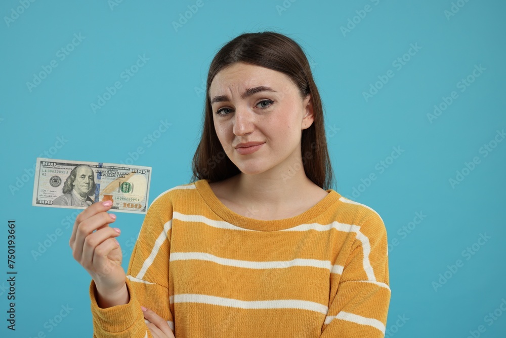 Sad woman with dollar banknote on light blue background Sad woman with dollar banknote on light blue background