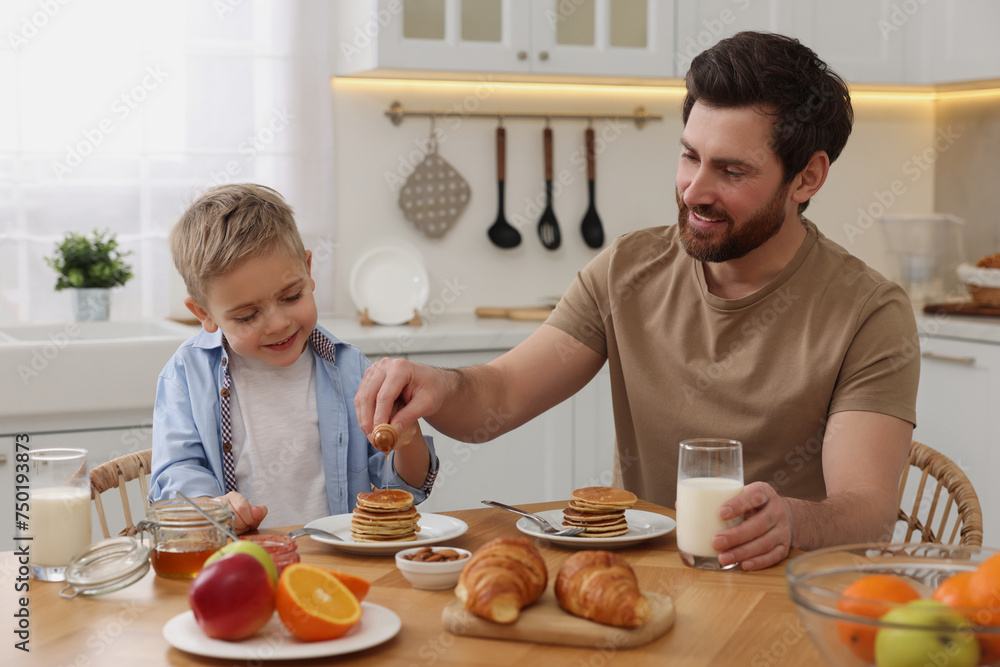 Father and his cute little son having breakfast at table in kitchen Father and his cute little son having breakfast at table in kitchen