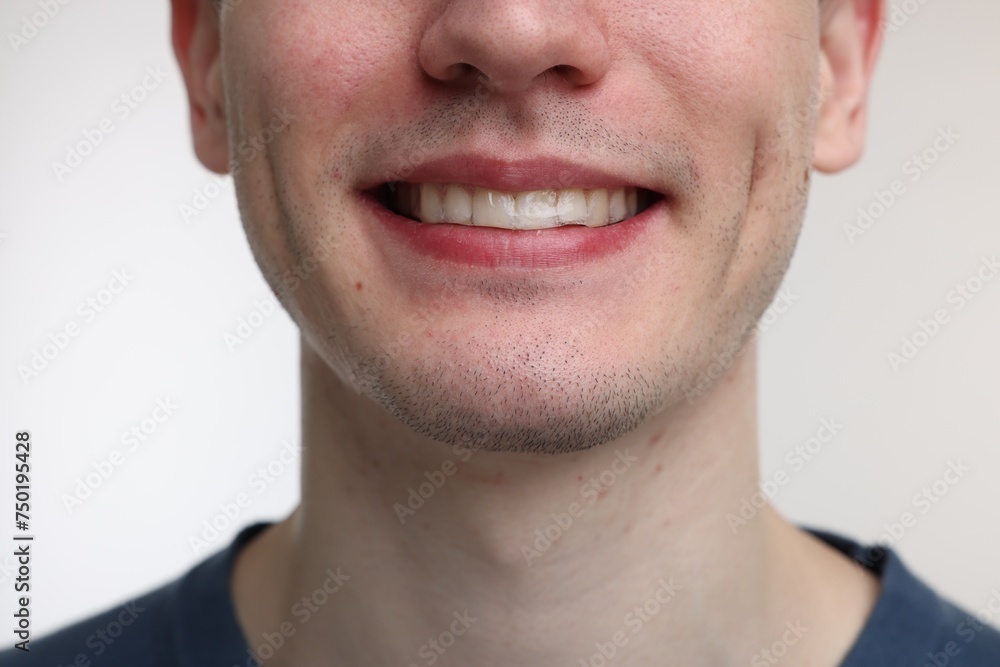 Fototapeta premium Young man using whitening strip on light background, closeup