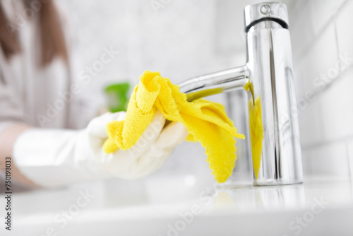 Close-up shot of woman in rubber gloves cleans the faucet with a rag and spray in the bathroom. Household and cleaning concept
