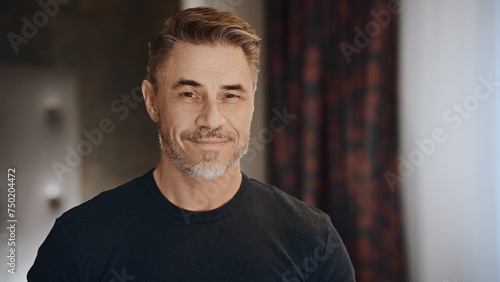 Portrait of a stylish, confident, and approachable middle-aged caucasian man with gray facial hair, wearing casual clothing, smiling and happy indoor at home.