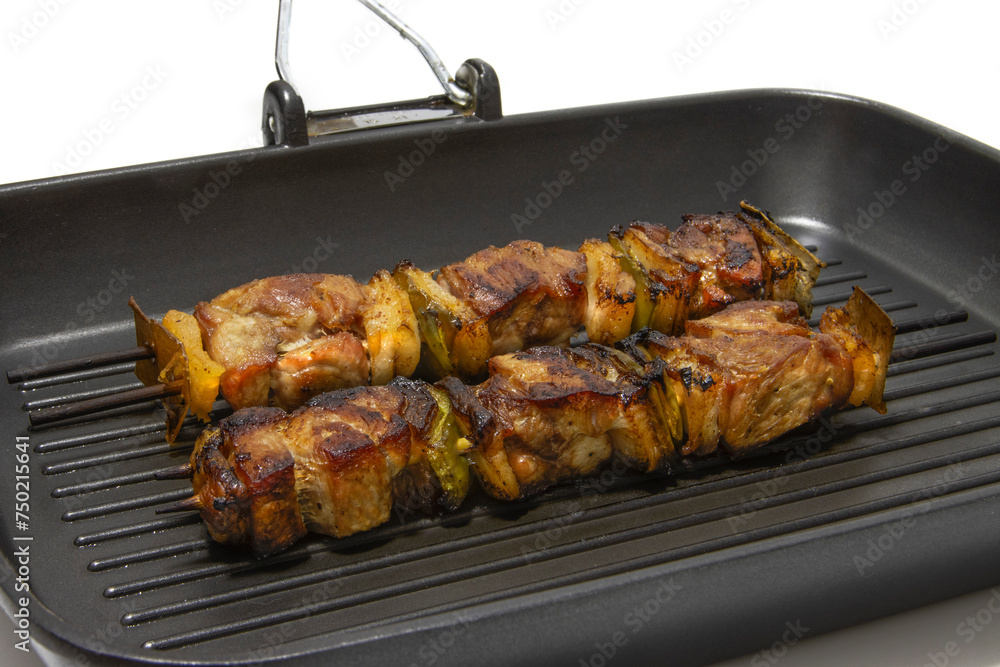 Meat and pepper skewers in a non-stick pan. Generally a skewer is made up of pieces of meat or fish interspersed with onion, pepper, mushrooms, etc.