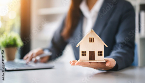 real estate agent's hand holds wooden house model on white table, symbolizing property investment and home ownership