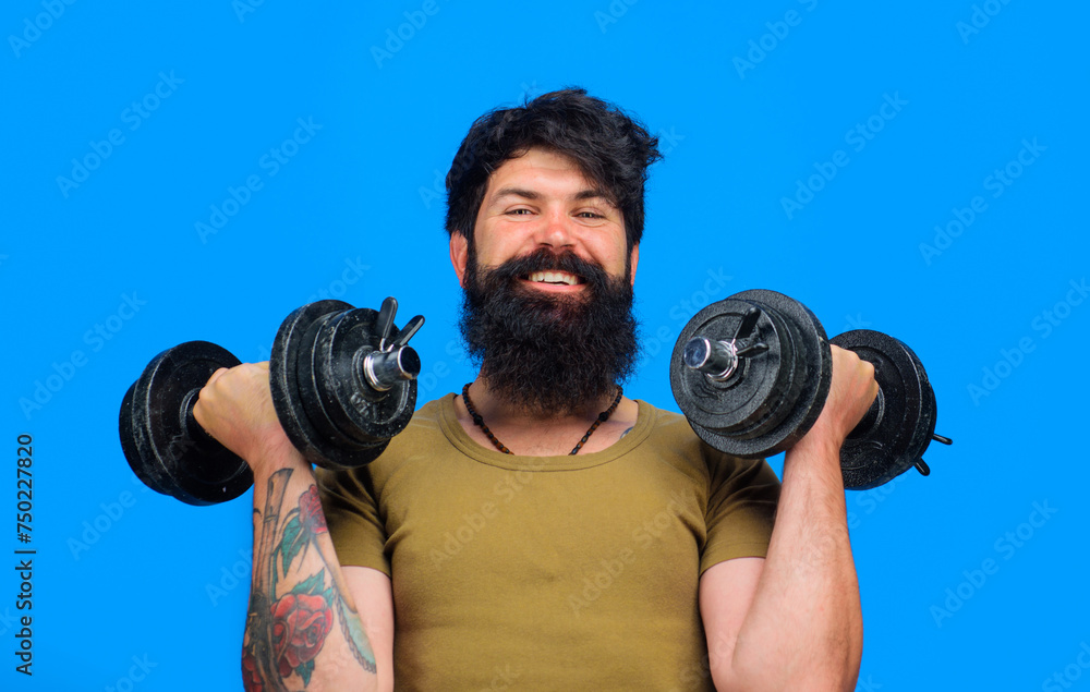 Smiling bearded man with dumbbells up in hands. Strong sportsman doing workout in fitness gym. Athletic muscular man lifting dumbbells in sport club. Weight training and bodybuilding. Sport equipment. Smiling bearded man with dumbbells up in hands. Strong sportsman doing workout in fitness gym. Athletic muscular man lifting dumbbells in sport club. Weight training and bodybuilding. Sport equipment.