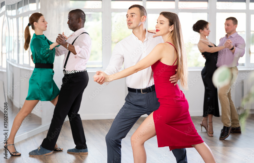 Fototapeta premium Dynamic young male and female attendees of dancing courses doing waltz in group