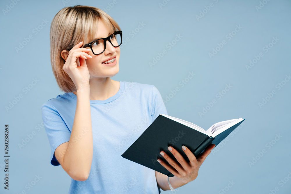 Smiling attractive young woman wearing eyeglasses holding book looking away on copy space Smiling attractive young woman wearing eyeglasses holding book looking away on copy space