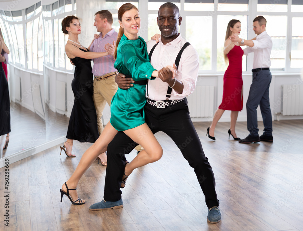 Positive middle-aged man and woman practicing waltz in pair in dancing studio