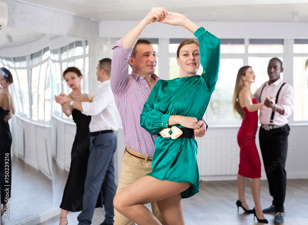Happy man and woman in elegant clothes performing ballroom dance in dancing room during celebration or party