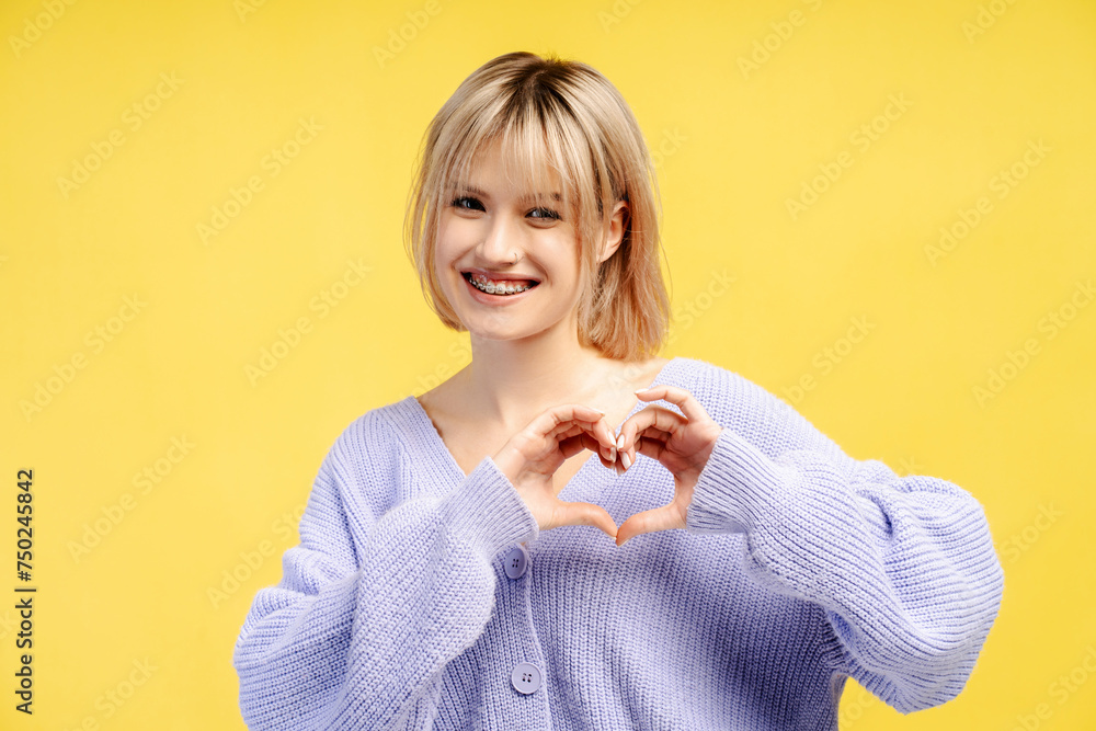 Happy smiling young woman wearing braces showing heart from hands, looking at camera, gesturing Happy smiling young woman wearing braces showing heart from hands, looking at camera, gesturing