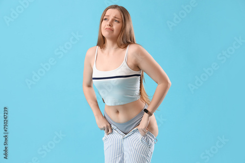 Upset young woman in tight jeans on blue background. Weight gain concept © Pixel-Shot