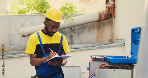 Knowleadgeable engineer doing leak checks and other necessary fixes to prevent major HVAC system failures. Efficient technician verifying air conditioner, writing findings on clipboard photo