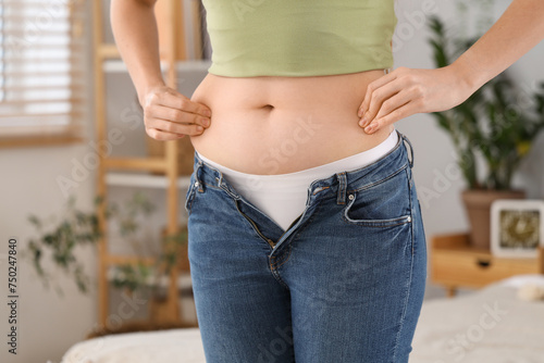 Young woman in tight jeans at home, closeup. Weight gain concept