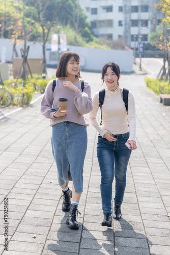 Two young Taiwanese female college students are walking happily talking on the university campus in Taipei, Taiwan. 台湾台北の大学キャンパスで二人の若い台湾人女性の大学生が楽しそうに話しながら歩いている © Hello UG