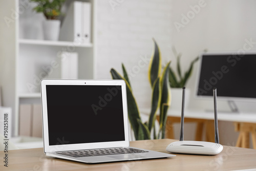 Modern wi-fi router with blank laptop on table in office