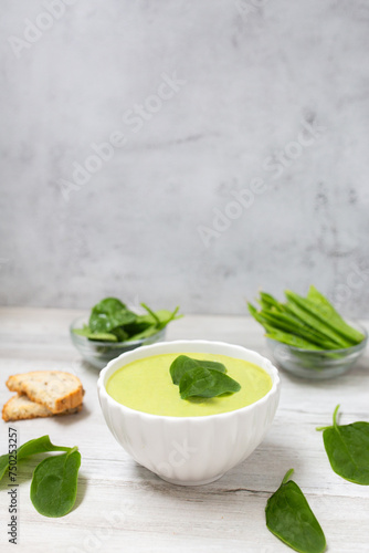 Homemade spinach cream soup in white bowl with bread on white wooden background. 