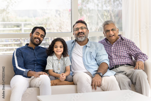 Happy little child, father, grandpa, great granddad sitting on home sofa together, looking at camera with toothy smiles, laughing, enjoying family meeting, leisure, relationship, friendship
