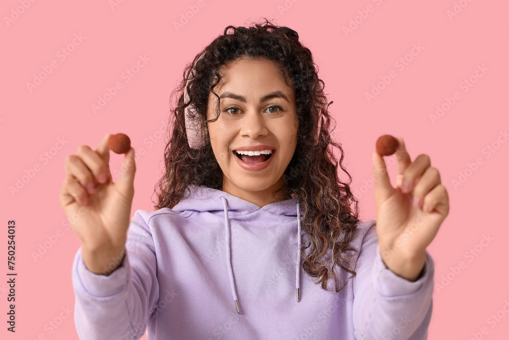Happy young African-American woman in headphones with sweet chocolate candies on pink background Happy young African-American woman in headphones with sweet chocolate candies on pink background