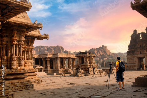 A male tourist photographer at the ancient stone architecture ruins of Vijaya Vittala temple at Hampi, Karnataka, India with moody sunset sky. 
