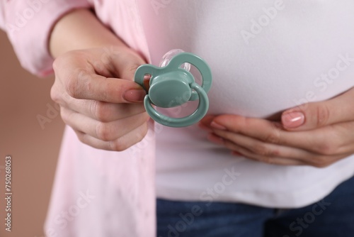 Pregnant woman holding pacifier on beige background, closeup